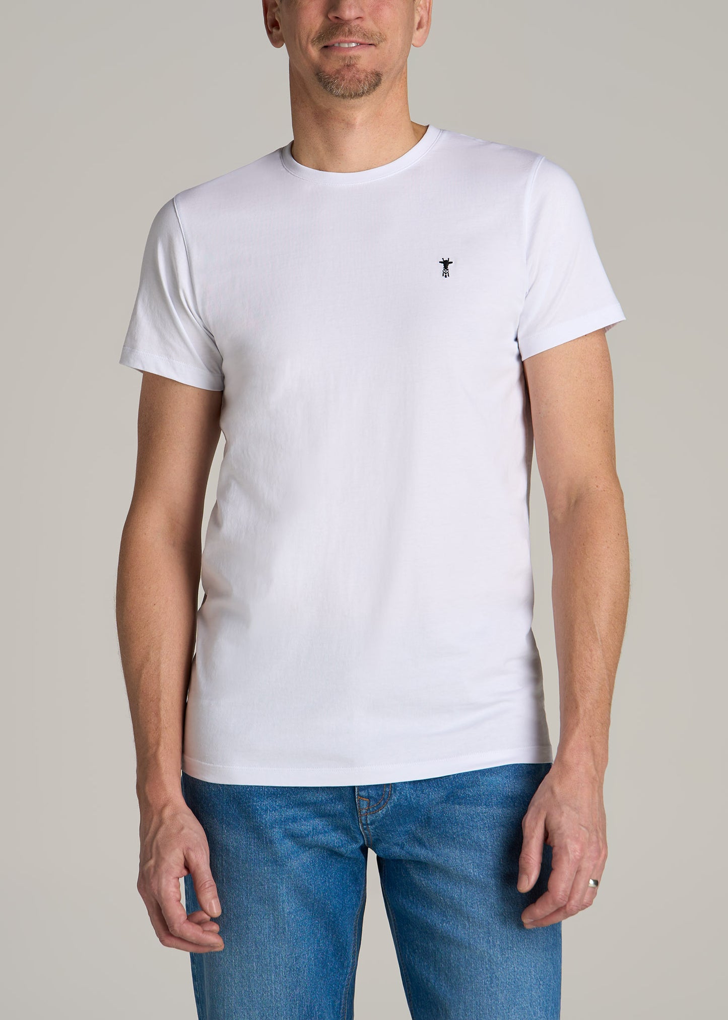 A tall man wearing American Tall's MODERN-FIT Embroidered Logo Crewneck T-Shirt for Tall Men in White